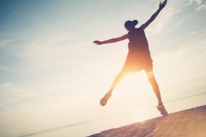 Silhouette of pretty woman jumping near ocean. Spending good time and fun. Intentional sun glare and lens flare effect, vintage color